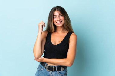 Mavi arka planda izole edilmiş genç beyaz kadın gülüyor.