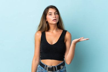 Mavi arka planda izole edilmiş genç beyaz kadın şüpheli hareketler yapıyor.