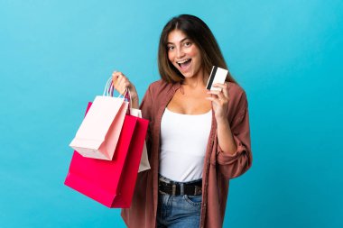 Mavi arka planda izole edilmiş beyaz bir kadın elinde alışveriş çantaları ve bir kredi kartı tutuyor.