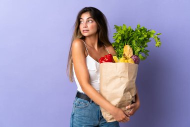 Market poşeti tutan genç bir kadın yan tarafa bakıyor.