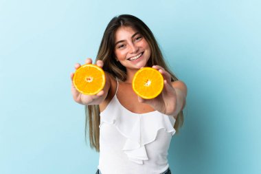 Mavi arka planda izole edilmiş beyaz bir kadın elinde bir portakal tutuyor.