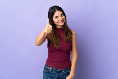 Genç beyaz kadın mor arka planda izole edildi. Başparmakları havada çünkü iyi bir şey oldu.