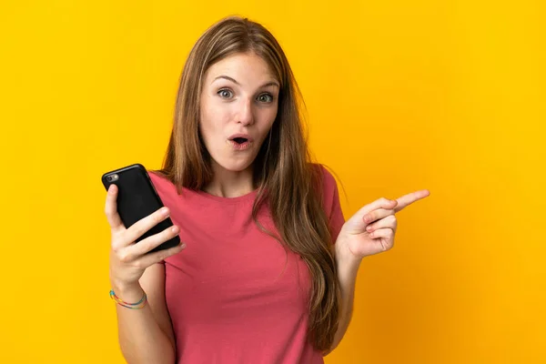 Mujer Joven Usando Teléfono Móvil Aislado Fondo Amarillo Sorprendido Señalando —  Fotos de Stock