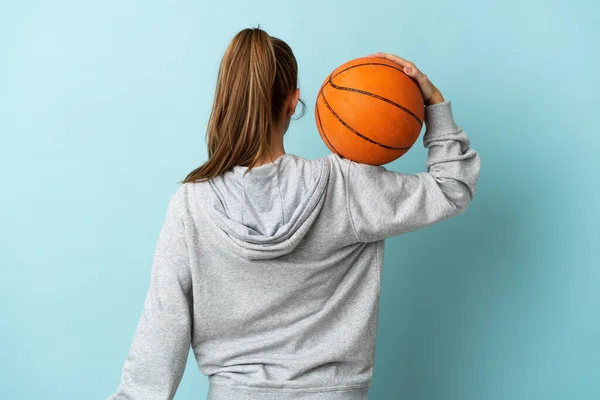 若いですCaucasian女性隔離上の青の背景プレーバスケットボールで背部位置 — ストック写真