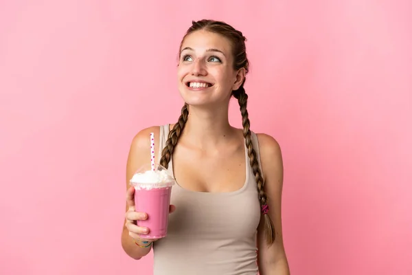 有草莓奶昔的年轻女子被粉色背景隔离 抬头看的时候想出了个主意 — 图库照片