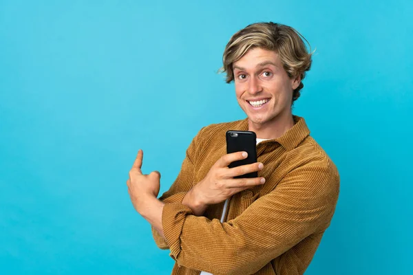 英语男子在孤立的蓝色背景上使用手机和指向后 — 图库照片