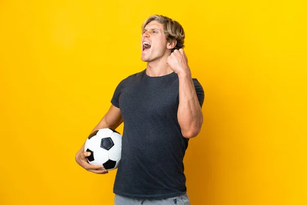 English man over isolated yellow background with soccer ball celebrating a victory