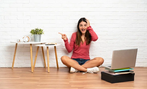 Young Woman Laptop Sitting Floor Indoors Surprised Pointing Finger Side — Foto Stock