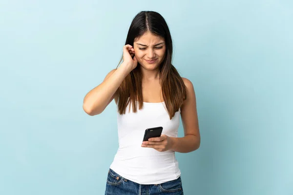青い背景に孤立した携帯電話を使用して若い白人女性フラストレーションとカバー耳 — ストック写真