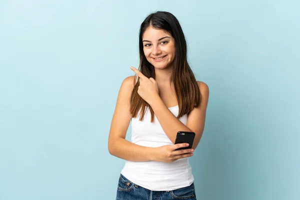 Молода Біла Жінка Використовує Мобільний Телефон Ізольовано Синьому Фоні Вказуючи — стокове фото