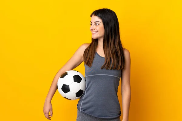 Young football player woman isolated on yellow background looking side