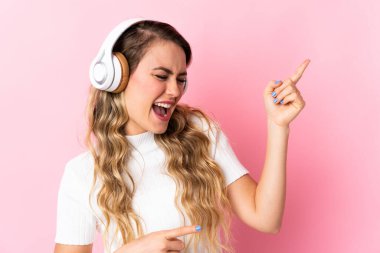 Young brazilian woman isolated on pink background listening music and doing guitar gesture