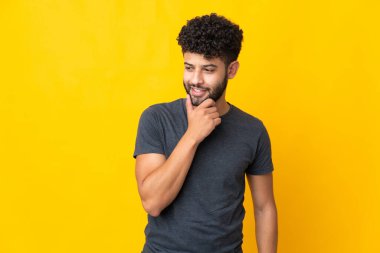Sarı arka planda izole edilmiş genç Faslı adam yana bakıyor ve gülümsüyor.
