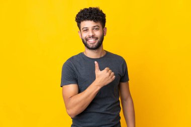 Faslı genç adam sarı arka planda izole edilmiş bir şekilde baş parmak hareketi yapıyor.