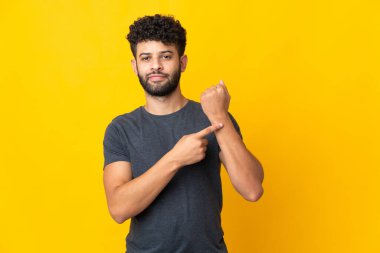 Genç Faslı adam sarı arka planda izole edilmiş. Geç kalma jesti yapıyor.