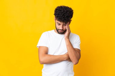 Faslı genç bir adam sarı arka planda izole edilmiş, baş ağrısı var.