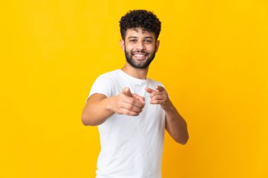 Young Moroccan man isolated on yellow background pointing to the front and smiling
