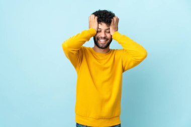 Genç Faslı adam mavi arka planda izole edilmiş gülüyor.