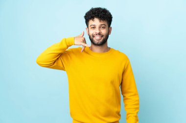 Young Moroccan man isolated on blue background making phone gesture. Call me back sign