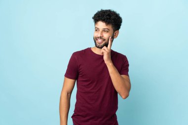 Genç Faslı bir adam mavi arka planda izole edilmiş bir şekilde bakarken bir fikir düşünüyor.