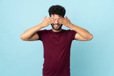 Faslı genç bir adam mavi arka planda izole edilmiş. Gözleri kapalı ve gülümsüyor.