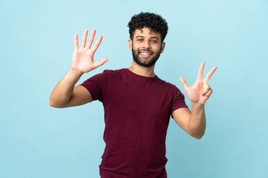 Faslı genç bir adam mavi arka planda izole edilmiş, parmaklarıyla sekiz kişi sayıyor.