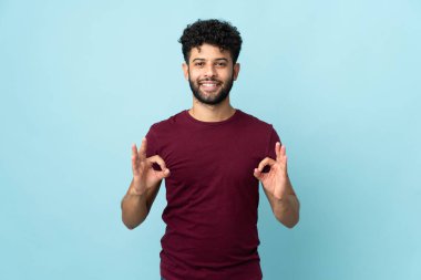 Young Moroccan man isolated on blue background showing ok sign with two hands