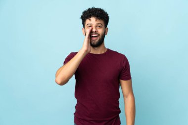 Faslı genç bir adam mavi arka planda izole edilmiş ağzı açık bağırıyor.