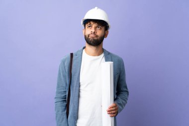 Young architect Moroccan man with helmet and holding blueprints over isolated background and looking up