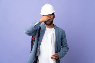 Young architect Moroccan man with helmet and holding blueprints over isolated background covering eyes by hands. Do not want to see something