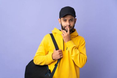 Young sport Moroccan man with sport bag isolated on purple background having doubts while looking up