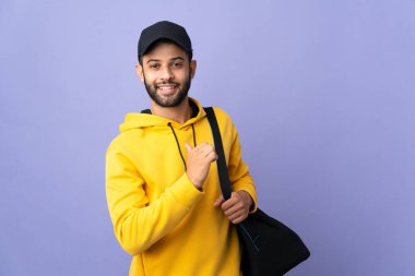 Young sport Moroccan man with sport bag isolated on purple background proud and self-satisfied