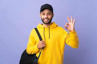 Young sport Moroccan man with sport bag isolated on purple background showing ok sign with fingers