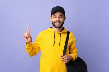 Young sport Moroccan man with sport bag isolated on purple background showing and lifting a finger in sign of the best