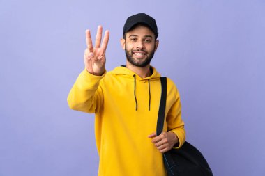 Young sport Moroccan man with sport bag isolated on purple background happy and counting three with fingers