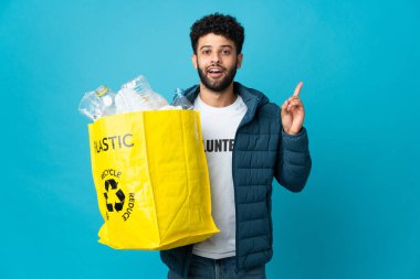 Elinde plastik şişelerle dolu bir çanta tutan genç Faslı adam izole edilmiş arka planda geri dönüşüm yapmak için çözümü bulmak için parmağını kaldırıyor.