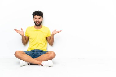 Young Moroccan handsome man sitting on the floor over isolated background with shocked facial expression