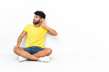 Genç Faslı yakışıklı adam izole bir zeminde oturuyor ve kulağına bir şeyler dinliyor.