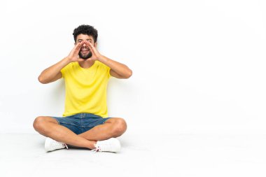 Young Moroccan handsome man sitting on the floor over isolated background shouting and announcing something