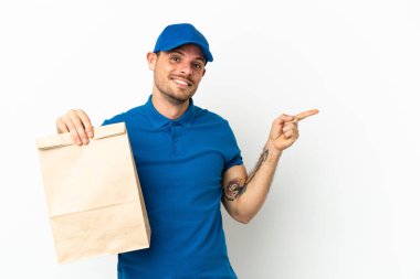 Brazilian taking a bag of takeaway food isolated on white background pointing finger to the side