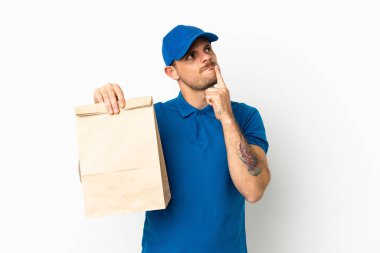 Brazilian taking a bag of takeaway food isolated on white background having doubts while looking up