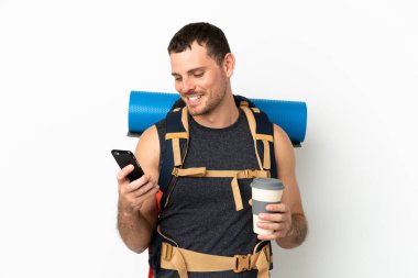 Brezilya 'lı dağcı, izole edilmiş beyaz arka plan üzerine büyük bir sırt çantası olan, elinde kahve ve bir cep telefonu olan bir adam.