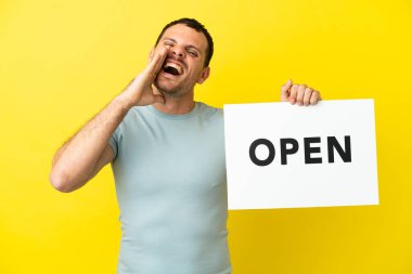 Brazilian man over isolated purple background holding a placard with text OPEN and shouting