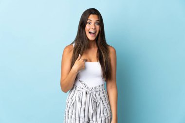 Genç Brezilyalı bir kadın mavi arka planda izole edilmiş ve yüzünde sürpriz bir ifade var.