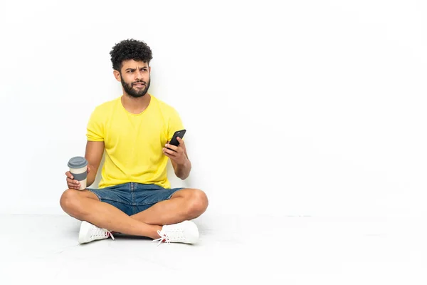 Young Moroccan Handsome Man Sitting Floor Isolated Background Holding Coffee — Φωτογραφία Αρχείου