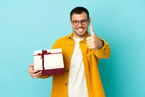 Brazilian Man Holding Gift Isolated Blue Background Thumbs Because Something — Stock Fotó