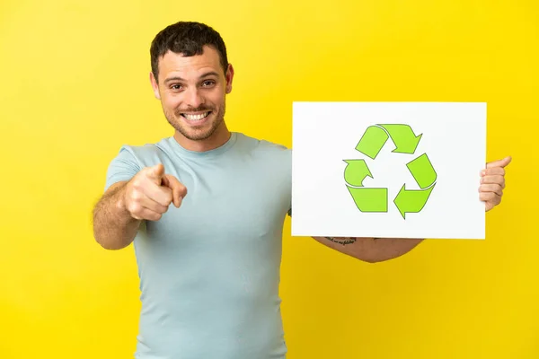 リサイクルアイコンとフロントを指すプラカードを保持孤立紫色の背景にブラジル人男性 — ストック写真