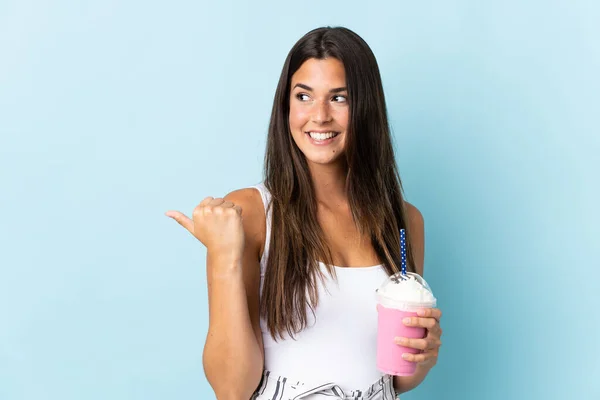 イチゴミルクシェイクを持つ若いブラジル人女性は 製品を提示する側を指している青の背景に隔離されました — ストック写真