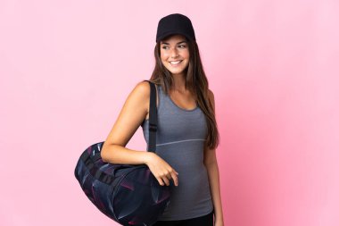 Pembe arka planda izole edilmiş spor çantalı genç Brezilyalı kız yana bakıyor ve gülümsüyor.