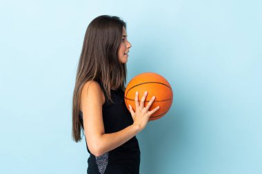 Mavi arka planda izole edilmiş genç Brezilyalı kız basketbol oynuyor.